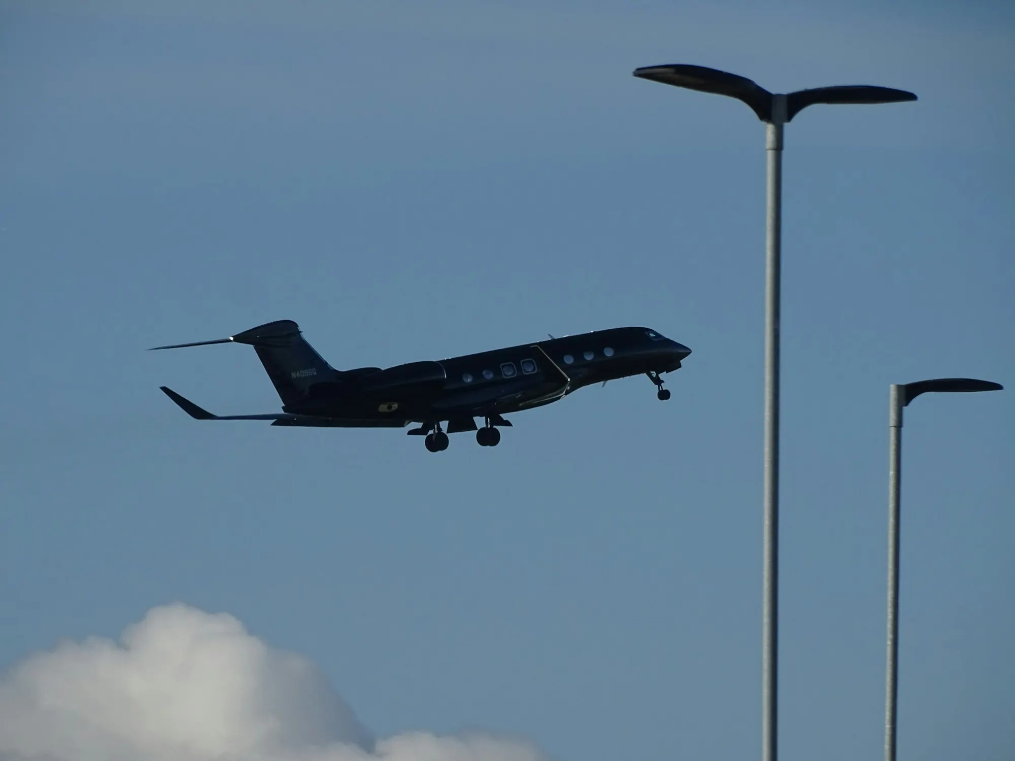 A business jet on final approach against a deep blue sky, framed by airport lights