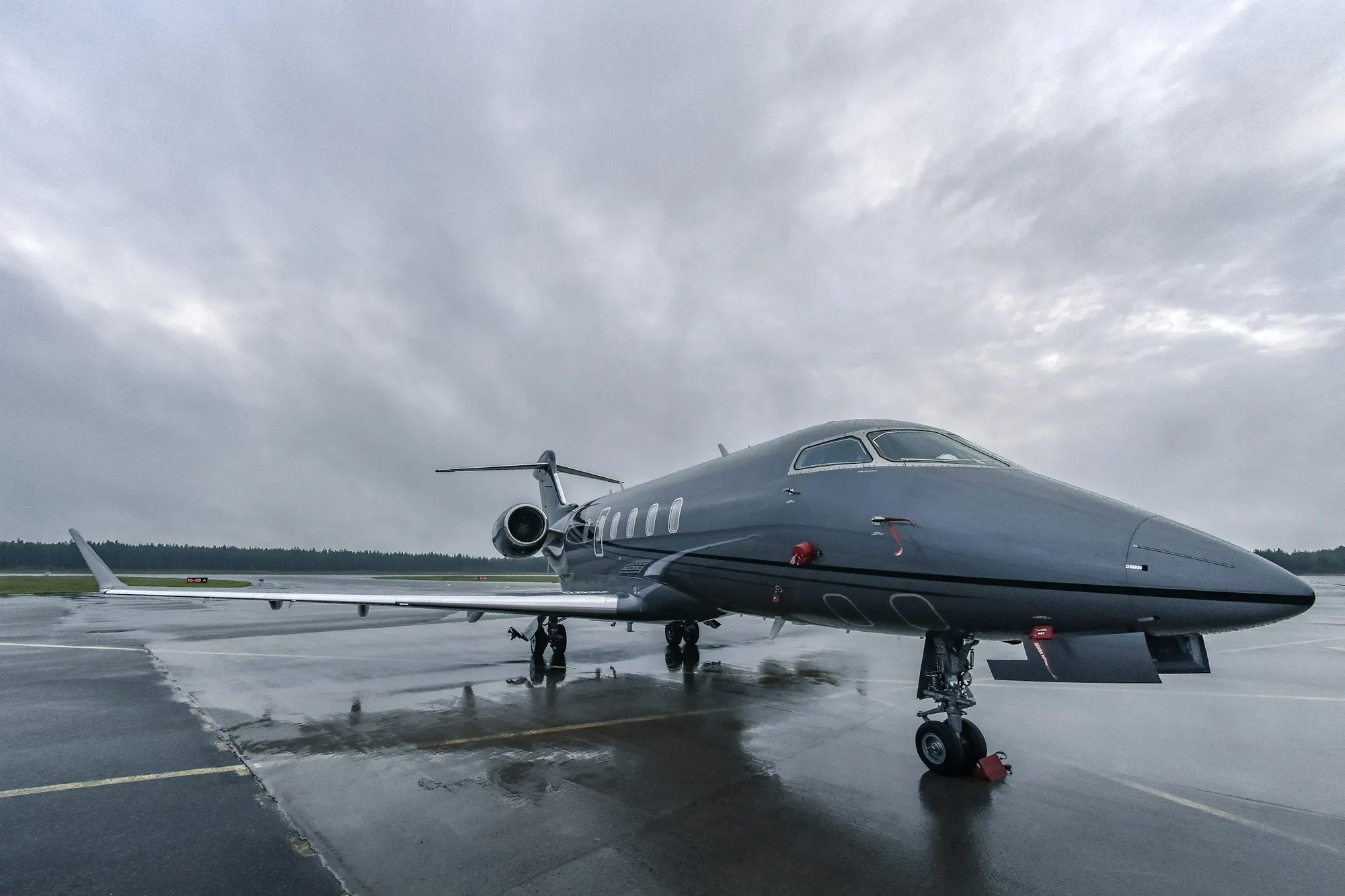 A grey business jet parked on a wet ramp under heavy cloud